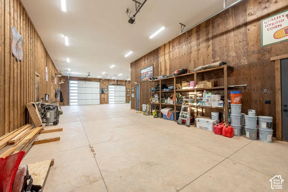 Spacious garage featuring two overhead doors, concrete flooring, exposed wood-finish walls, and ceiling-mounted strip lighting