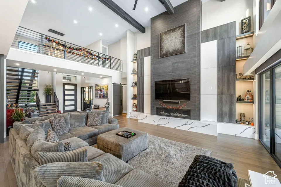Great room featuring a two-story ceiling with exposed beams, wood-finish flooring, and a multi-paneled fireplace surround with integrated shelving