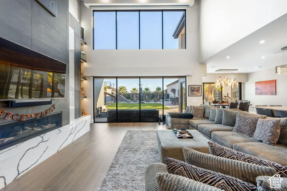Great room featuring a two-story ceiling, wood-finish flooring, a contemporary fireplace with a stone surround, and floor-to-ceiling windows