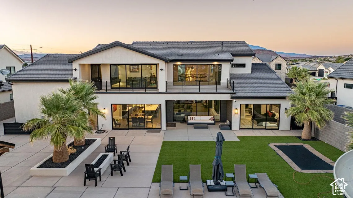 Modern stucco exterior with multiple balconies, expansive patio, artificial turf, integrated trampoline, and mature palm trees