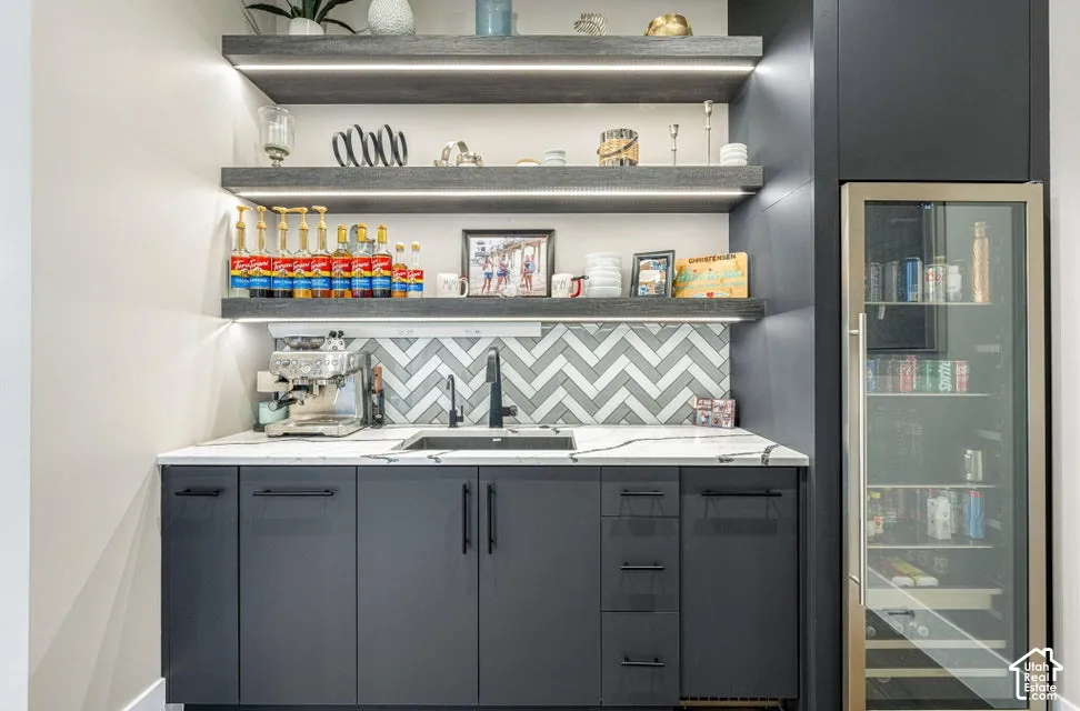 Built-in wet bar featuring dark cabinetry, white countertop, chevron pattern backsplash, integrated sink with matte black faucet, and under-cabinet lighting