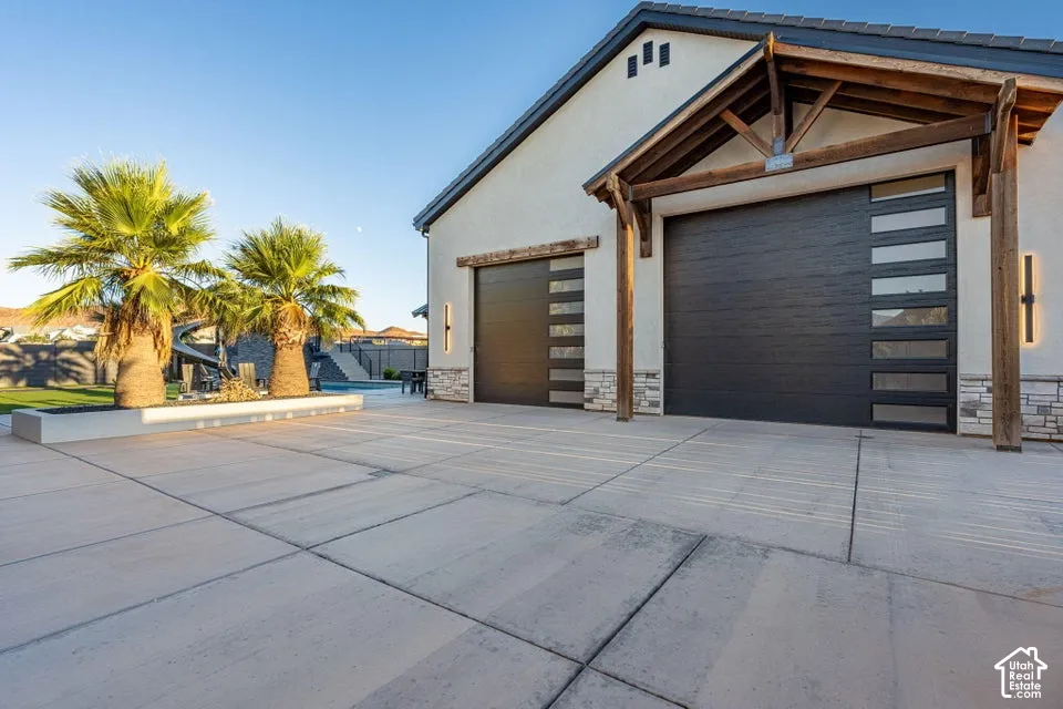 Spacious concrete driveway leading to a residence featuring a stucco exterior, stone accents, and two modern garage doors with frosted glass panels
