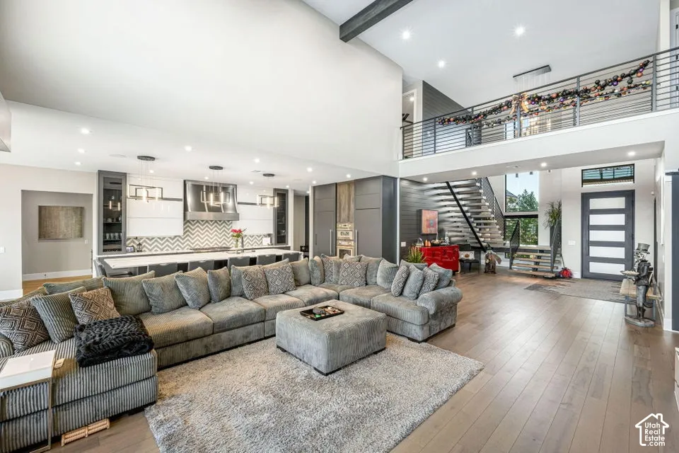 Open concept living space featuring wood-finish flooring, a contemporary kitchen with chevron tile backsplash, a floating staircase with glass railings, a second-story balcony overlooking the living area, and a prominent entry door with horizontal glass p
