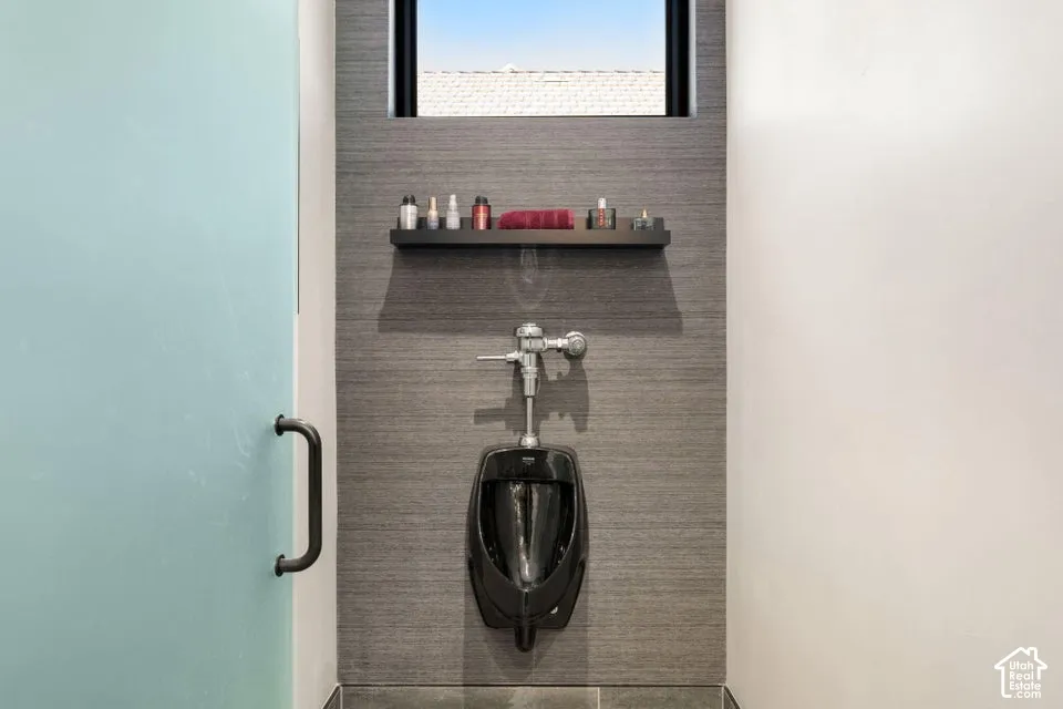 Frosted glass door with matte black handle, black urinal, textured wall paneling, small window, and built-in shelf