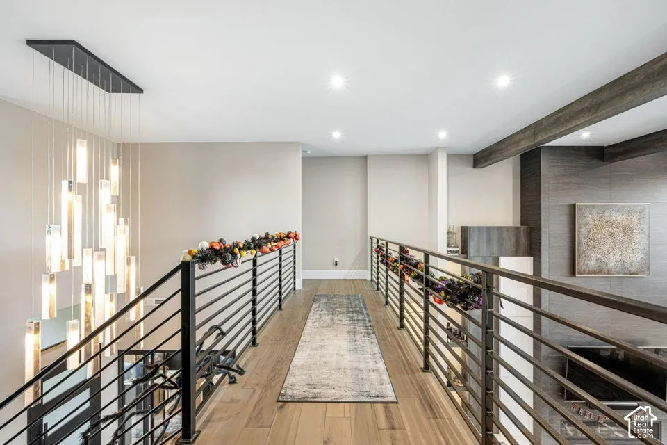 Modern chandelier over a staircase with metal railings, wood-finish flooring, recessed lighting, and a textured accent wall