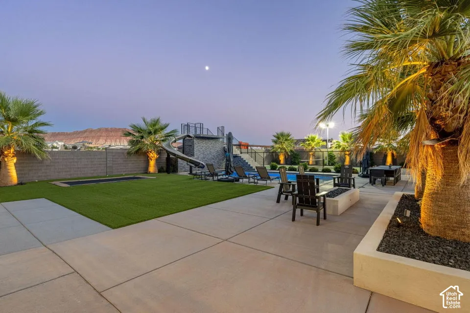 Hardscaped patio with an in-ground pool, fire pit, and a built-in slide structure