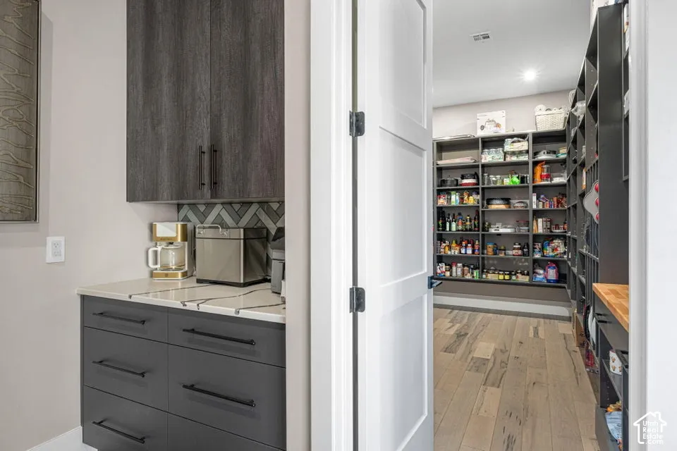 Modern kitchen and pantry featuring sleek dark cabinetry with integrated hardware, stainless steel appliances, and wood-finish flooring