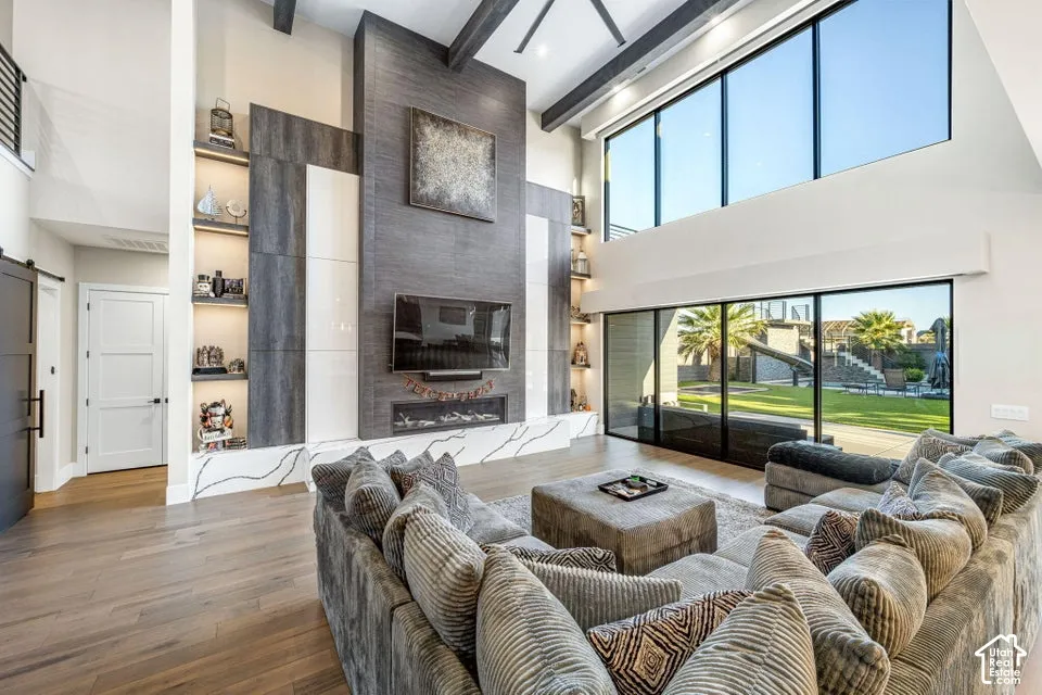 Living area with wood-finish flooring, a two-story fireplace with integrated shelving, and a vaulted ceiling with exposed beams