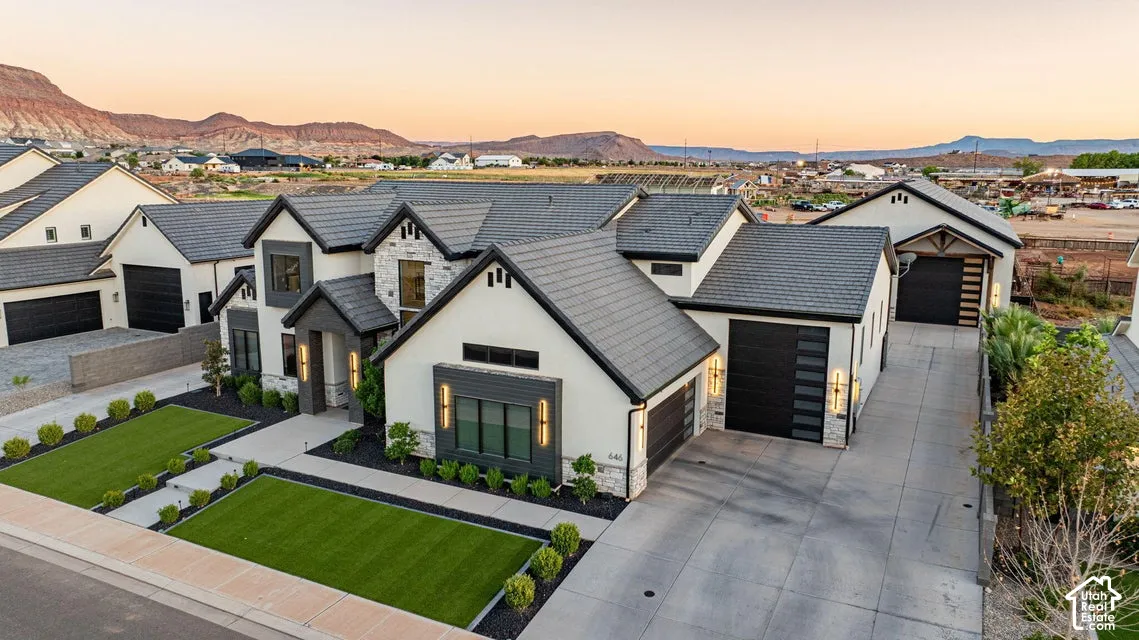 Contemporary exterior with a multi-level roofline, stone and stucco facade, multiple garage doors, and landscaped artificial turf