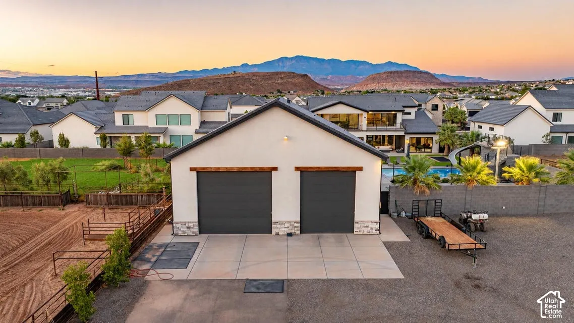 Spacious dual-bay garage with dark-finish overhead doors and concrete apron, situated on expansive grounds with manicured landscaping, fencing, and mountain vistas beyond the residential neighborhood backdrop