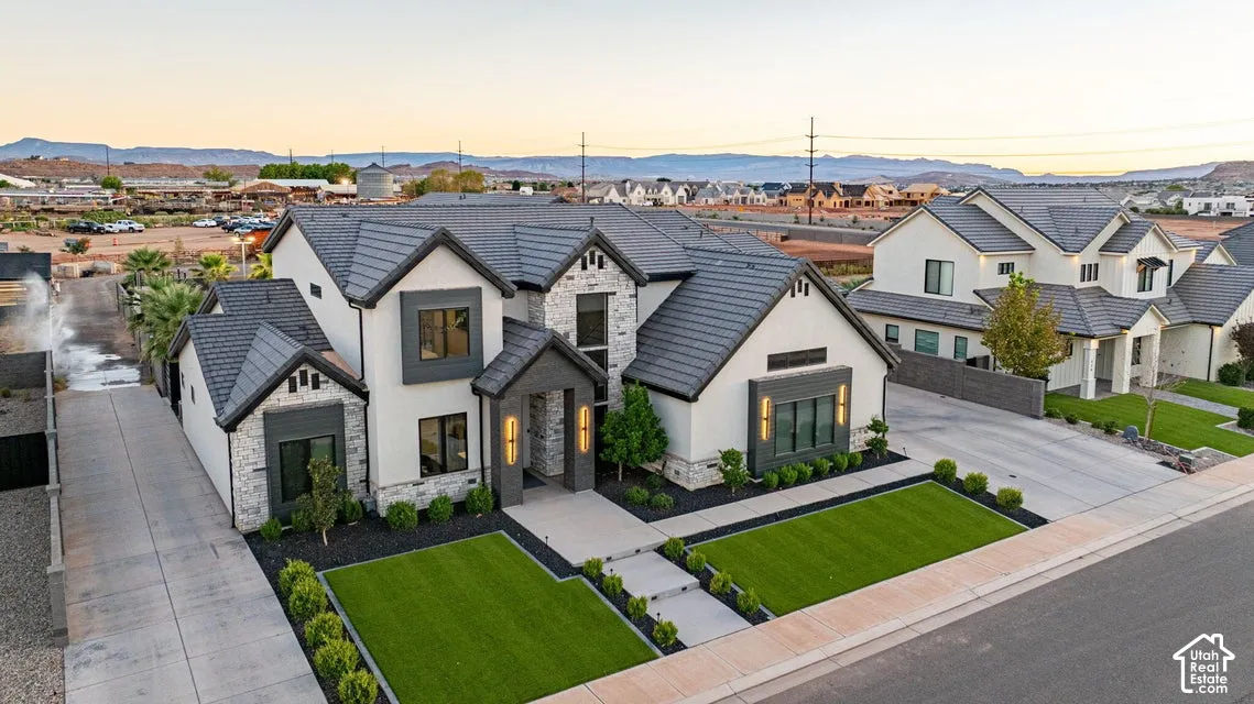 Contemporary exterior with stone accents, dark-framed windows, a dark tile roof, paved driveway, and manicured landscaping