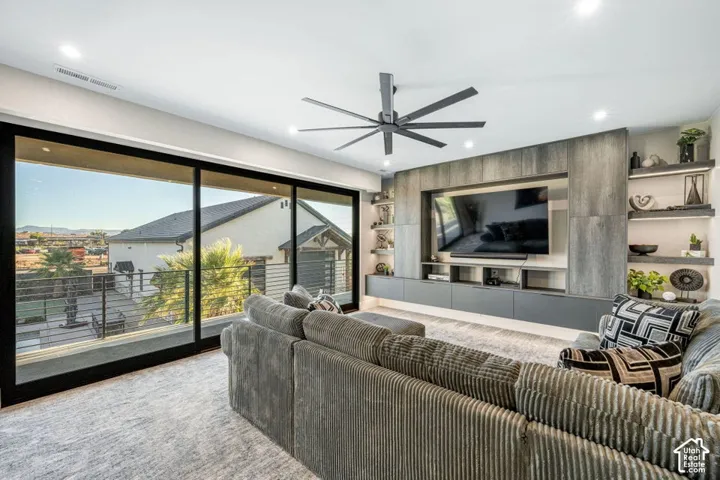 Wide sliding glass doors, built-in media console with integrated shelving, recessed lighting, and a modern ceiling fan