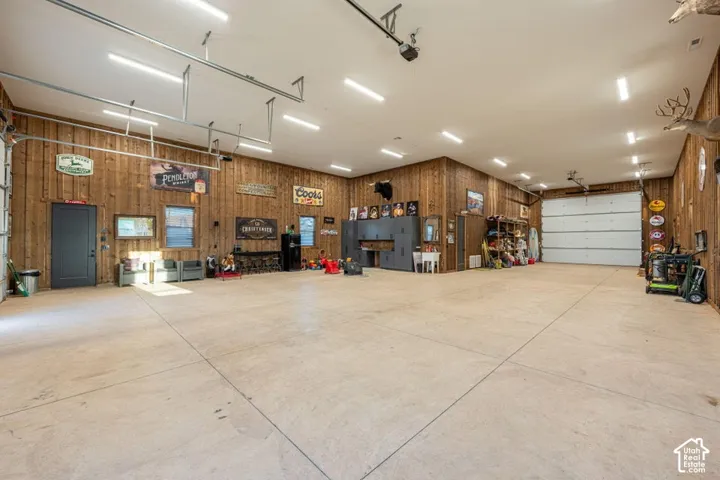Spacious garage with light-toned concrete flooring, wood-paneled walls, multiple garage doors, and abundant overhead lighting