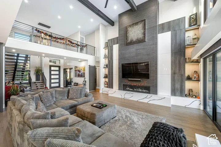 Great room featuring a two-story ceiling with exposed beams, wood-finish flooring, and a multi-paneled fireplace surround with integrated shelving