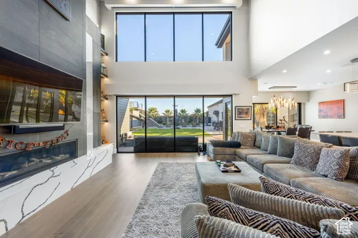 Great room featuring a two-story ceiling, wood-finish flooring, a contemporary fireplace with a stone surround, and floor-to-ceiling windows
