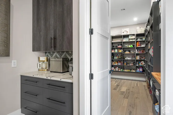 Modern kitchen and pantry featuring sleek dark cabinetry with integrated hardware, stainless steel appliances, and wood-finish flooring
