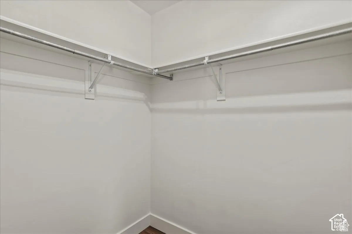 White walls defining a corner space with metal hanging rods and wood-finish flooring