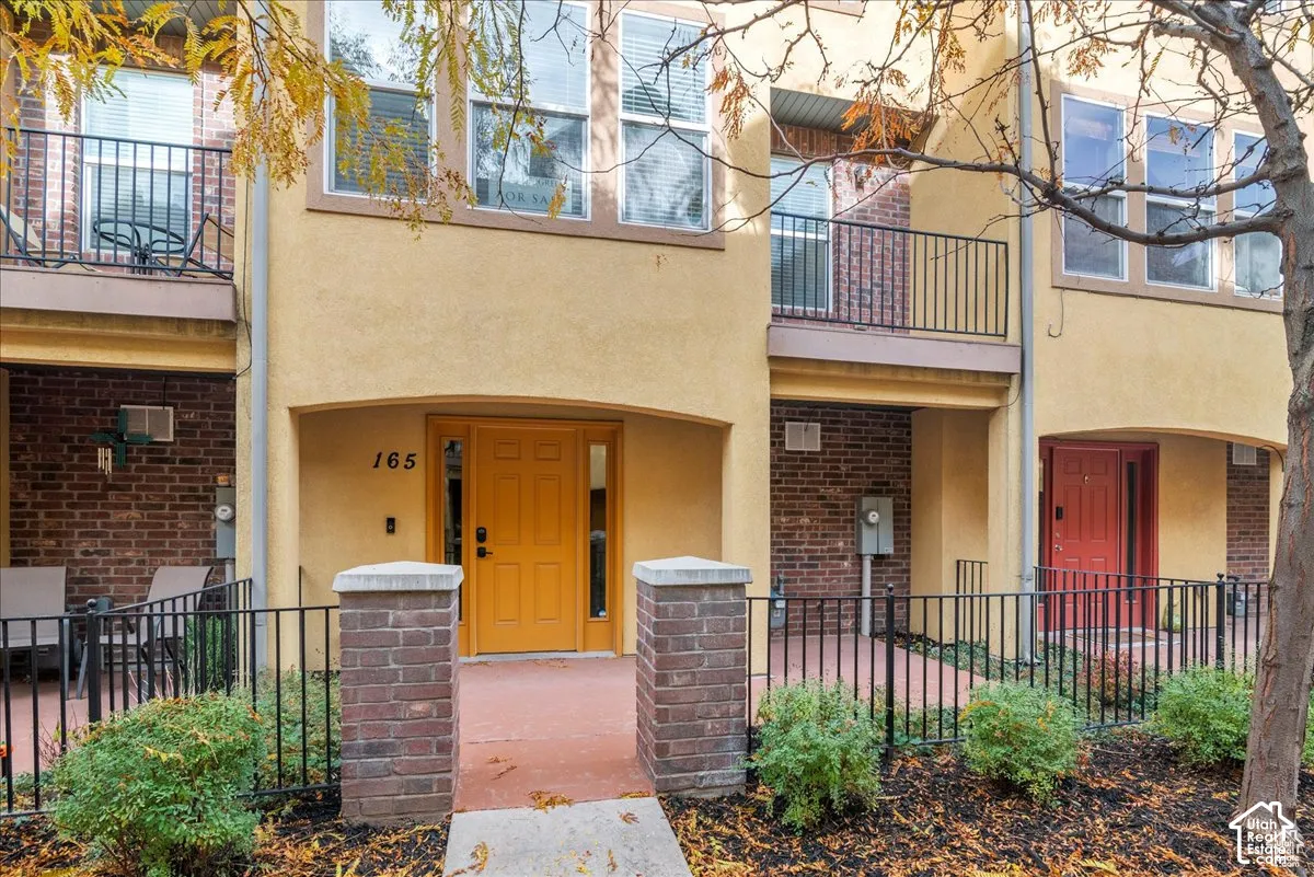Stucco exterior with brick accents, featuring an arched entry, a vibrant yellow front door, and a private balcony with wrought iron railing
