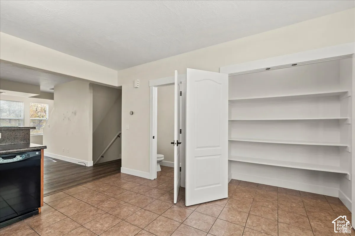 Tile flooring, built-in shelving, black dishwasher, and dark wood-finish flooring