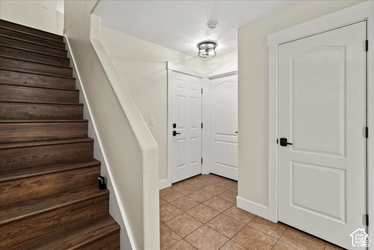 Wood-finish staircase, tile flooring, white interior doors, and a semi-flush mount light fixture