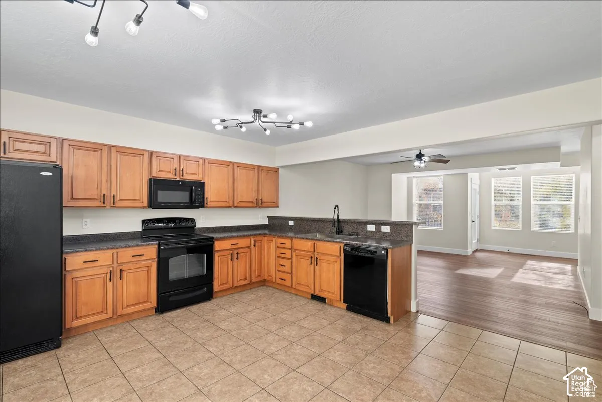 Kitchen featuring wood cabinetry, black appliances, a stone-finish countertop, and tile flooring