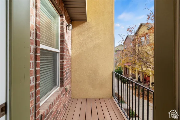 Private balcony with wood-finish decking, black iron railing, stucco exterior, and brick accent wall