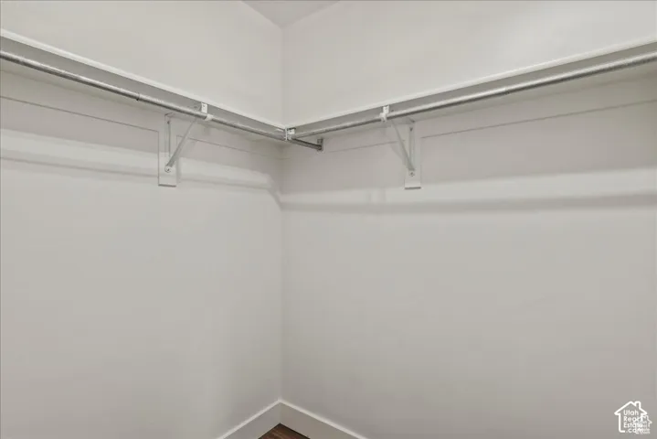 White walls defining a corner space with metal hanging rods and wood-finish flooring