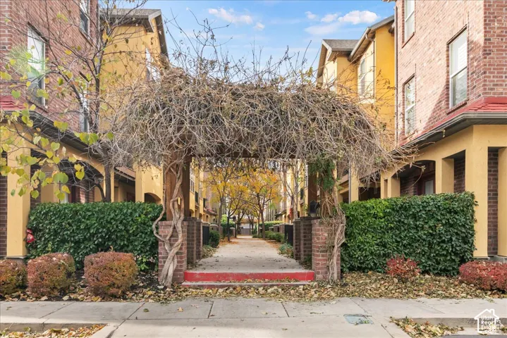 Arched wooden trellis entry with mature vine coverage, brick-clad columns, and a paved walkway