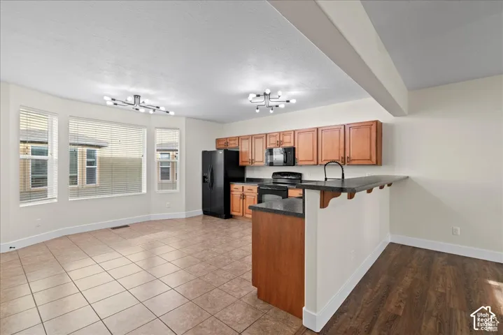Kitchen featuring wood cabinetry, black appliances, dark countertops, and a peninsula with seating space