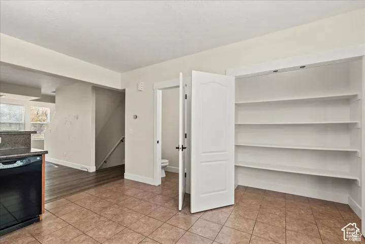 Tile flooring, built-in shelving, black dishwasher, and dark wood-finish flooring