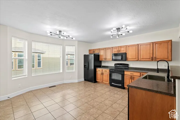 Kitchen featuring wood cabinetry, black appliances, dark countertops, a double basin sink, and tile flooring