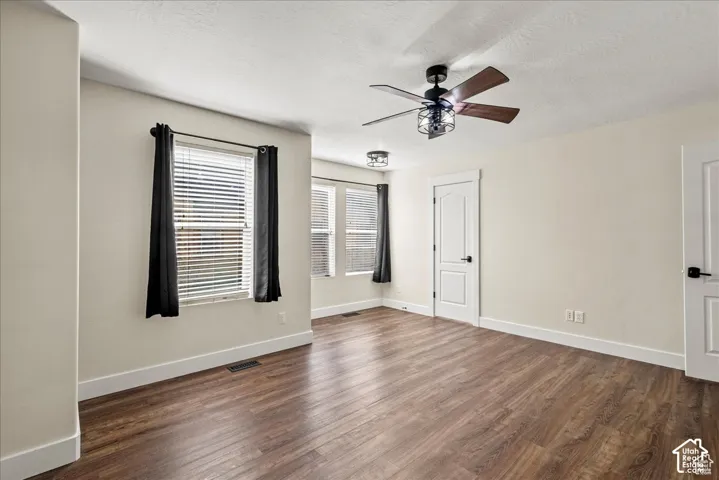Master bedroom.  Wood-finish flooring, multiple windows with blinds, ceiling fan with integrated lighting, and white paneled doors with black hardware