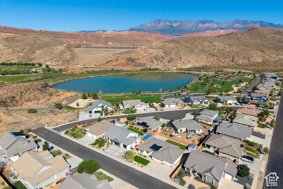 Residential development with paved streets and manicured landscaping, featuring a community lake and golf course in the background