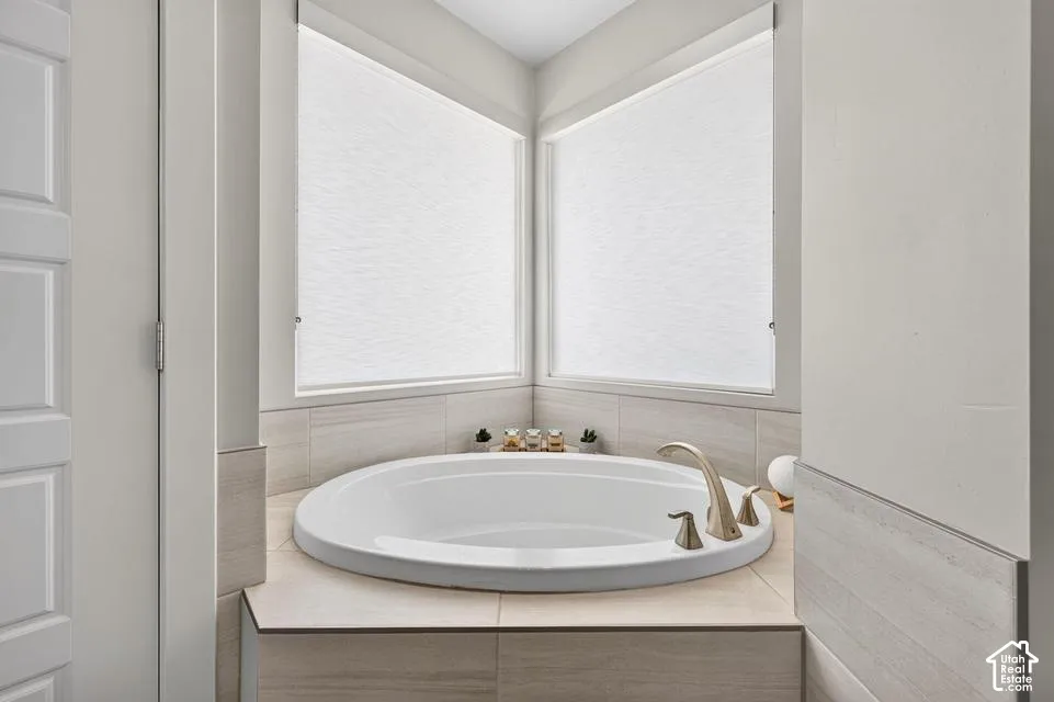 Built-in soaking tub with brushed nickel fixtures, surrounded by light-toned wall tile and under-window roller shades