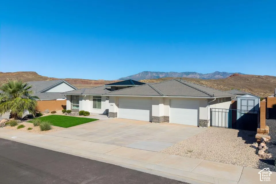 Contemporary stucco exterior with stone accents, a tiered gray shingle roof, and an attached two-car garage