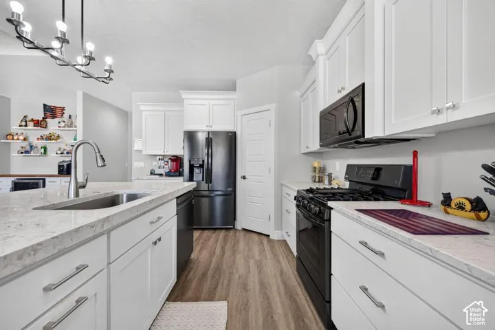 Kitchen featuring white cabinetry, light-toned countertops, a stainless steel sink, black appliances, and wood-finish flooring