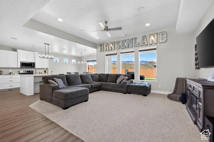 Open-concept living space with wood-finish flooring, a kitchen island with seating, a ceiling fan, and large windows