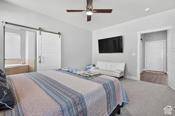 Tray ceiling with a ceiling fan, white barn door, and a built-in tub with wood-finish paneling