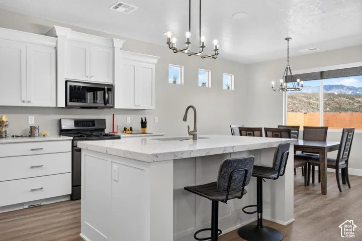 Well-appointed kitchen featuring white cabinetry, light-toned countertops, a central island with sink, and stainless steel appliances