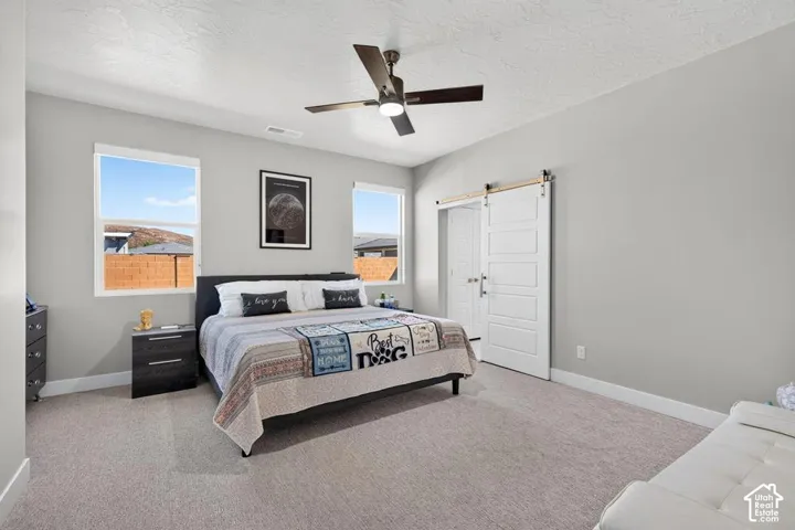 Spacious room with light gray walls, plush carpet flooring, two large windows, a ceiling fan, and a white barn door