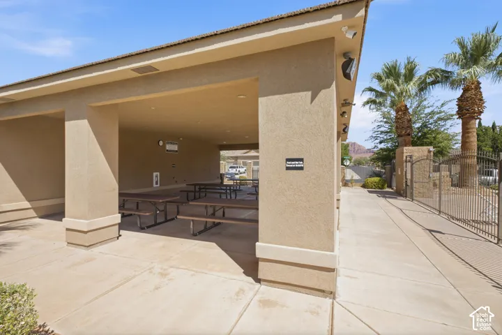 Covered outdoor structure with stucco exterior, concrete flooring, and an adjacent wrought iron gate