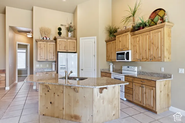 Kitchen featuring a central island with an integrated sink, light wood-finish cabinetry, speckled countertops, and tile flooring