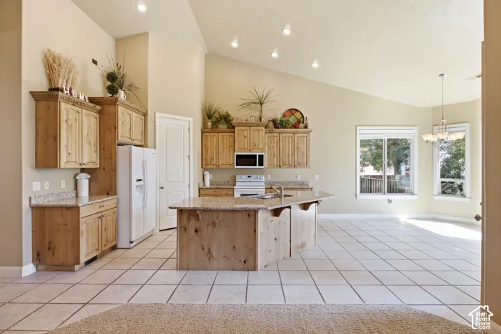 Vaulted ceilings with recessed lighting, light wood cabinetry, white appliances, and a central island with a built-in sink