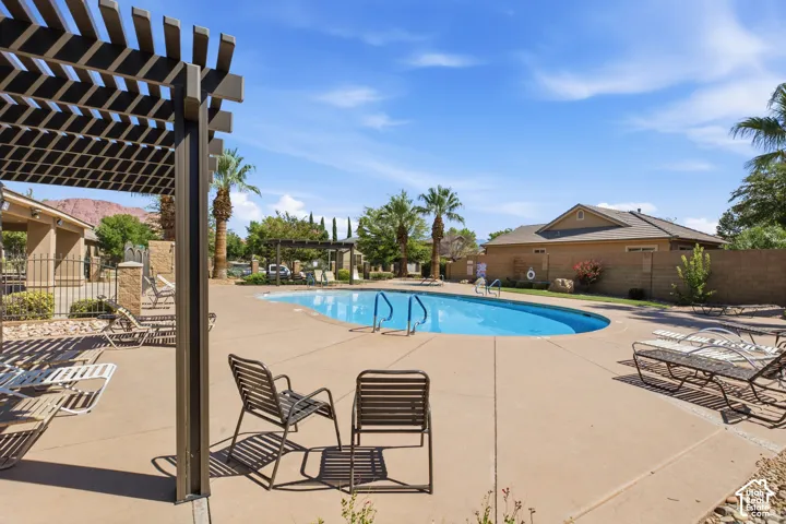 Outdoor swimming pool with concrete decking, surrounding buildings with stucco exteriors, and a slatted pergola structure