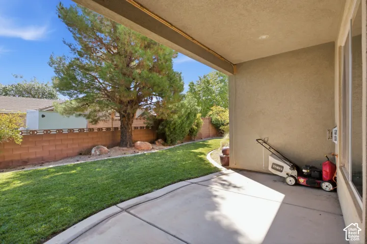 Covered patio with a concrete surface, surrounded by a manicured lawn and mature landscaping