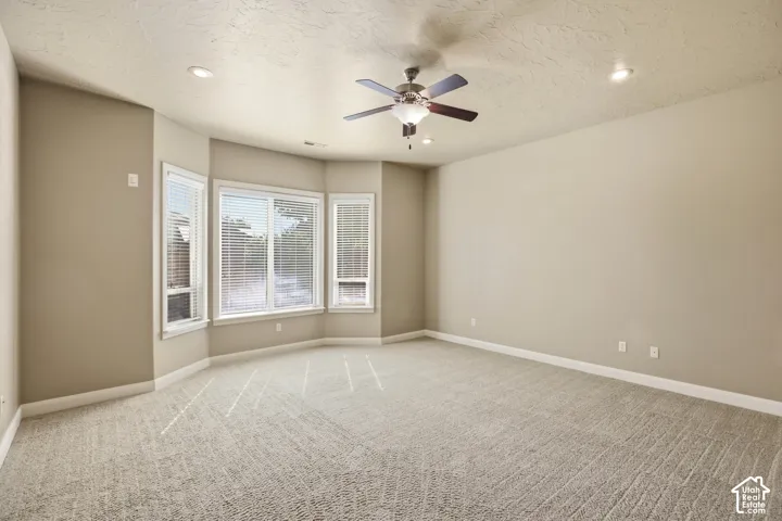 Bay window with multiple panes, ceiling fan with integrated lighting, recessed lighting, and textured carpeting