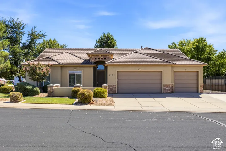 Stucco exterior with stone accents, a tile roof, an arched entry door, and a three-car garage