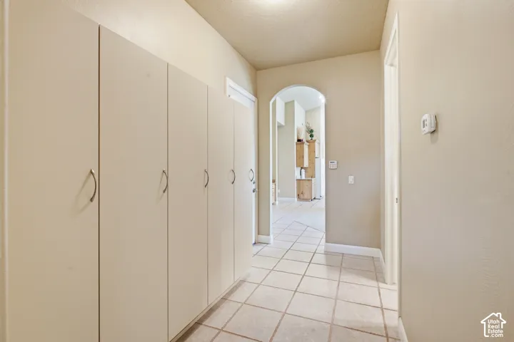 Full-height storage cabinetry with brushed nickel hardware, neutral-toned tile flooring, and an arched doorway