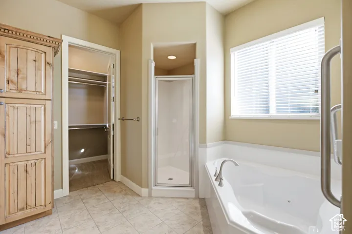 Tile flooring, built-in wooden storage cabinetry, enclosed shower, soaking tub, and a window with blinds