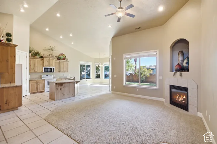 Vaulted ceilings with recessed lighting, an electric fireplace with a tiled surround, a kitchen with wood cabinetry, a central island, and white appliances, and a tiled dining area